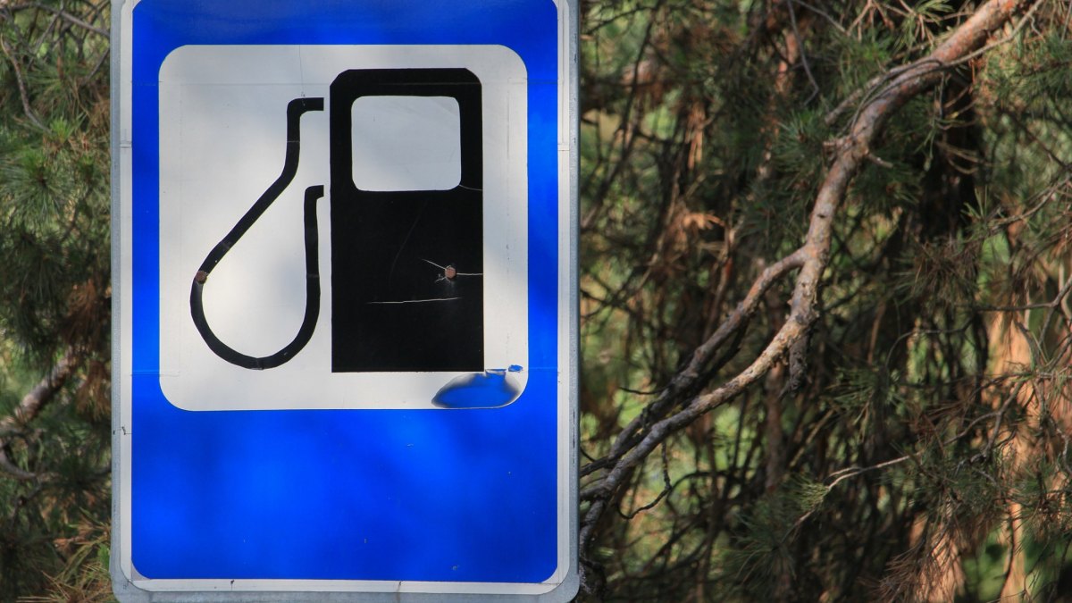 Old shabby European road sign indicating a gas station. Background