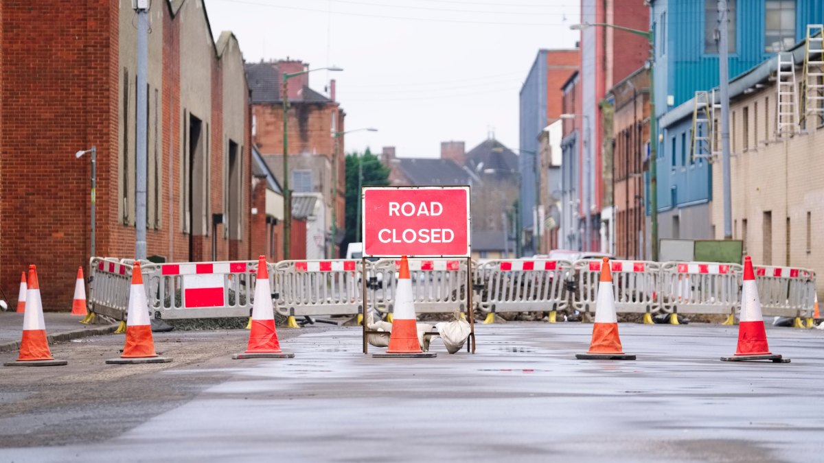 Road ahead closed sign with traffic cones and red barrier fence crossing